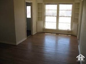 Lubbock Lease Homes: Empty room with hardwood floors, a large bay window letting in natural light, built-in shelves on both sides of the window, and an open doorway leading to another space.