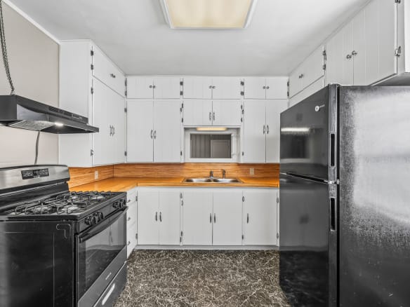 Lubbock Lease Homes: A kitchen with white cabinets, black appliances including a gas stove and refrigerator, a double sink under a small window, wood backsplash, and dark marble-patterned flooring.