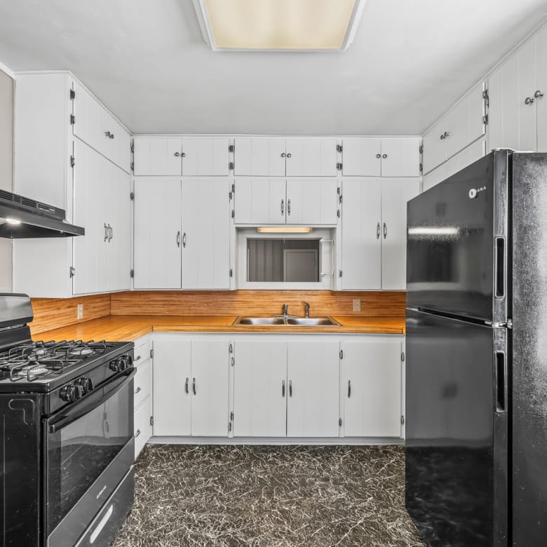 Lubbock Lease Homes: A kitchen with white cabinets, black appliances including a gas stove and refrigerator, a double sink under a small window, wood backsplash, and dark marble-patterned flooring.