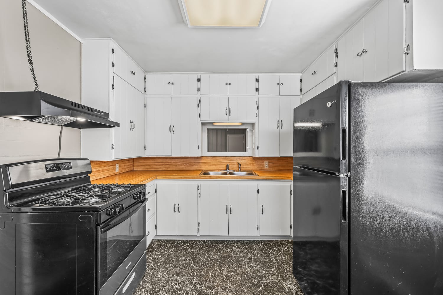 Lubbock Lease Homes: A kitchen with white cabinets, black appliances including a gas stove and refrigerator, a double sink under a small window, wood backsplash, and dark marble-patterned flooring.
