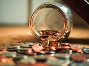 Lubbock Lease Homes: A glass jar tipped over on its side, spilling various coins, including pennies, nickels, and quarters—an image reflecting the everyday budgeting amid the cost of living in Lubbock.