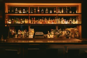 Lubbock Lease Homes: A dimly lit bar with a variety of liquor bottles arranged on illuminated shelves behind the counter, bar stools in front, and bar equipment and glasses neatly organized on the countertop.