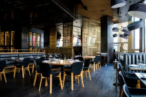Lubbock Lease Homes: Modern restaurant interior with wooden tables, black chairs, and large windows letting in natural light. Stylish and welcoming, this spot is a standout among Lubbock restaurants for its elegant lighting, dark floors, and variety of seating options.