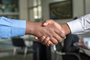Lubbock Lease Homes: Two people in business attire shake hands in an office setting, symbolizing agreement or partnership. The background is blurred, showing office furniture and a wall with a framed picture.
